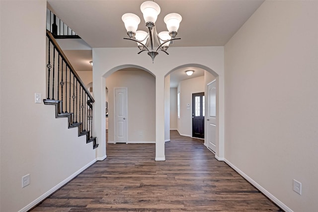 foyer featuring baseboards, arched walkways, dark wood-style flooring, stairs, and a notable chandelier