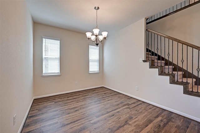 spare room featuring dark wood-style floors, baseboards, stairway, and a notable chandelier