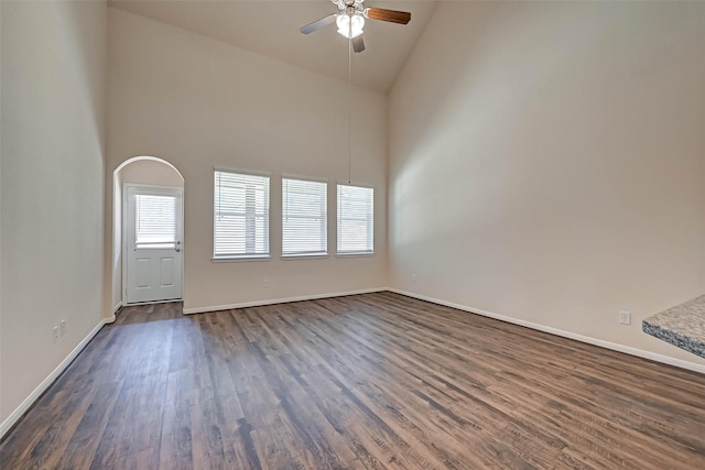 empty room with a ceiling fan, dark wood finished floors, high vaulted ceiling, and baseboards