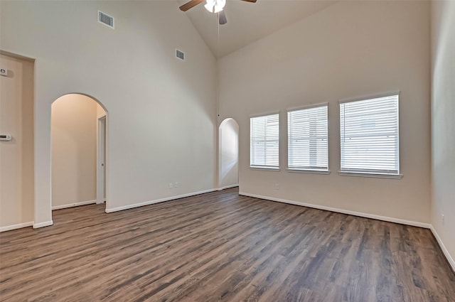 empty room featuring arched walkways, ceiling fan, high vaulted ceiling, dark wood-type flooring, and visible vents