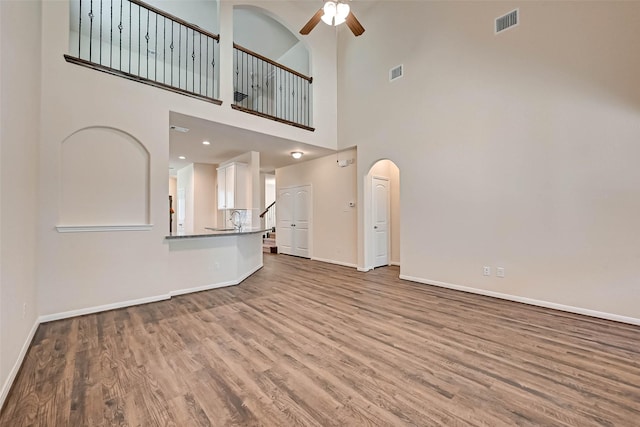 unfurnished living room featuring baseboards, visible vents, arched walkways, and wood finished floors