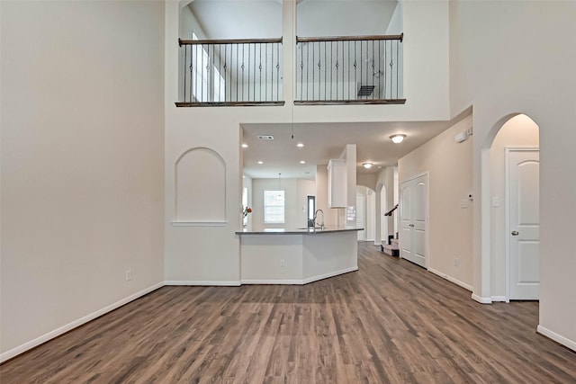 unfurnished living room with arched walkways, dark wood-type flooring, and baseboards