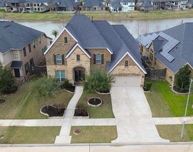 view of front of property with a shingled roof, concrete driveway, a water view, a residential view, and stone siding