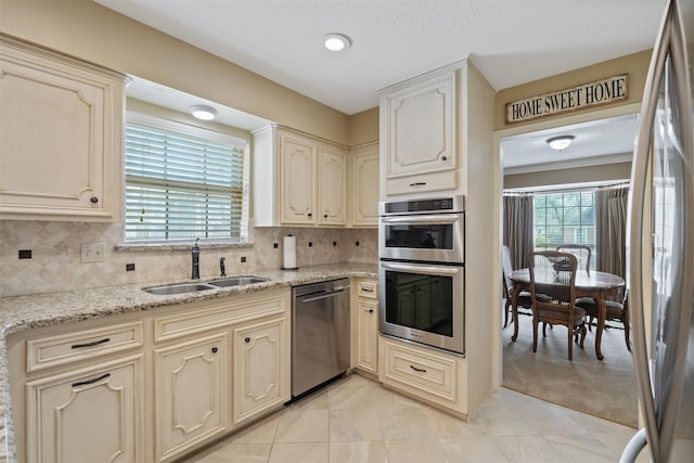 kitchen with appliances with stainless steel finishes, a sink, decorative backsplash, and cream cabinets