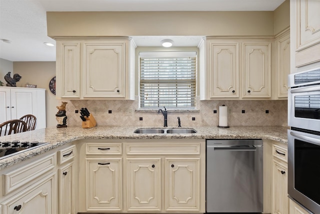 kitchen with light stone counters, cream cabinetry, decorative backsplash, appliances with stainless steel finishes, and a sink