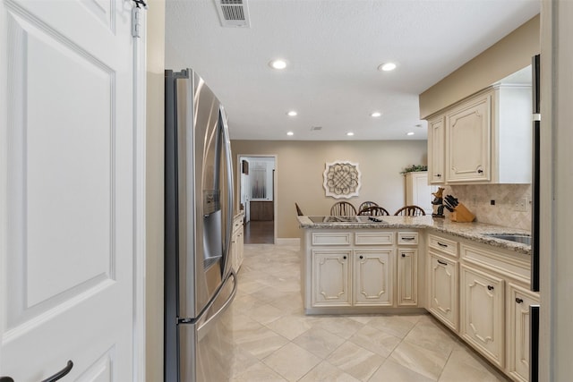 kitchen with cream cabinetry, visible vents, stainless steel refrigerator with ice dispenser, and a peninsula