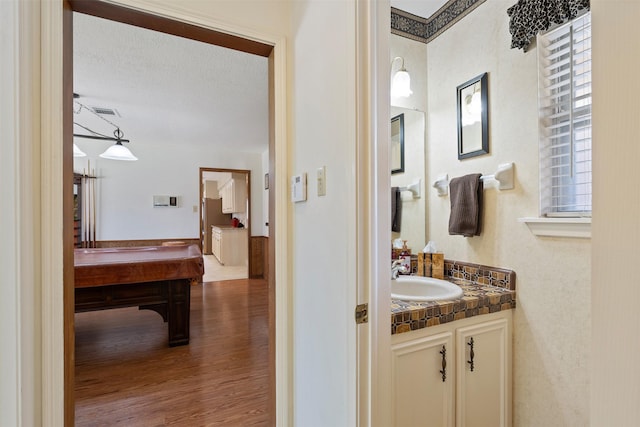 bathroom with a textured ceiling, wood finished floors, visible vents, billiards, and vanity