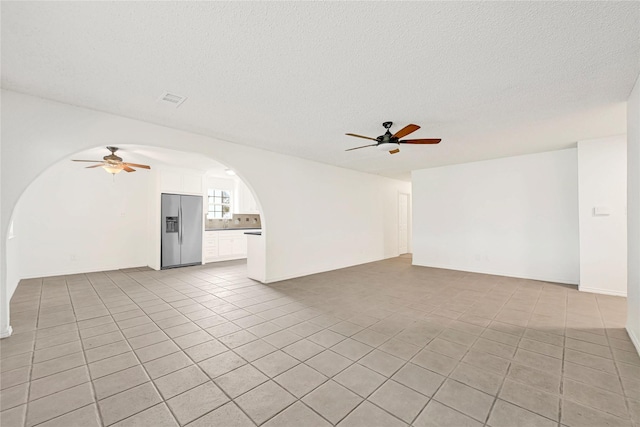 unfurnished living room featuring arched walkways, visible vents, light tile patterned flooring, ceiling fan, and a textured ceiling