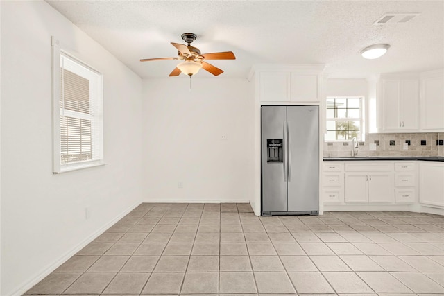 kitchen featuring a sink, visible vents, white cabinetry, stainless steel refrigerator with ice dispenser, and dark countertops