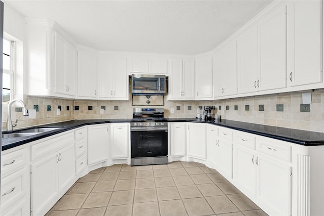 kitchen featuring stainless steel appliances, dark countertops, decorative backsplash, white cabinetry, and a sink