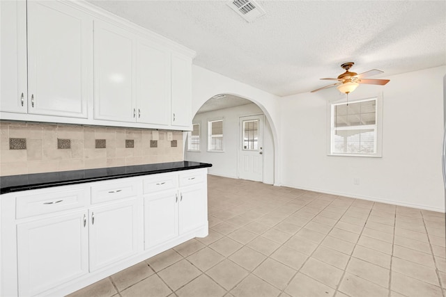 kitchen with tasteful backsplash, visible vents, arched walkways, dark countertops, and white cabinetry