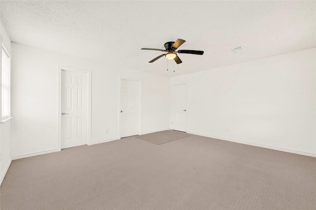 empty room with a textured ceiling, carpet flooring, a ceiling fan, visible vents, and baseboards