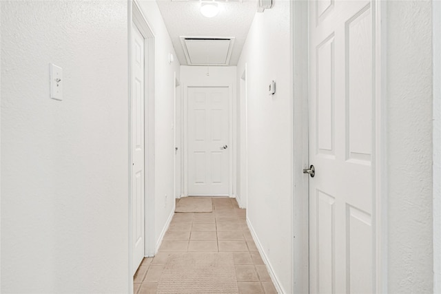 corridor featuring light tile patterned floors, a textured ceiling, attic access, and baseboards