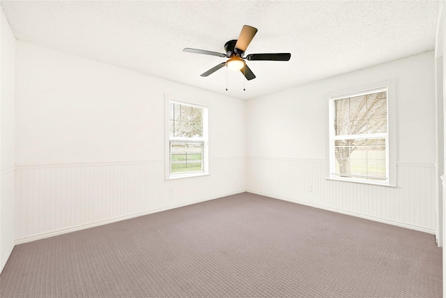 spare room with a wainscoted wall, ceiling fan, a textured ceiling, and carpet flooring