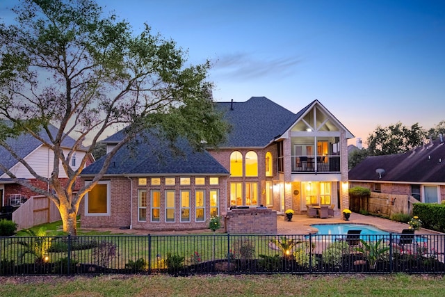 back of house at dusk featuring a patio area, a fenced backyard, and a balcony