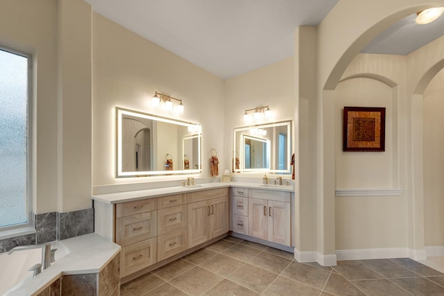 full bath with double vanity, tiled tub, tile patterned flooring, and a sink