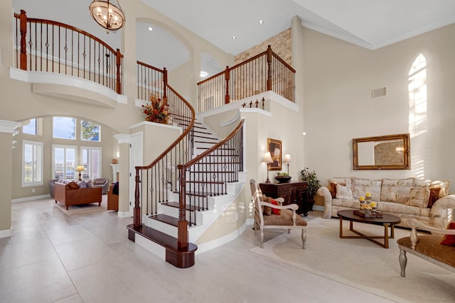 staircase with crown molding, ornate columns, visible vents, an inviting chandelier, and baseboards