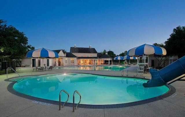 pool featuring a water slide, a patio area, and fence