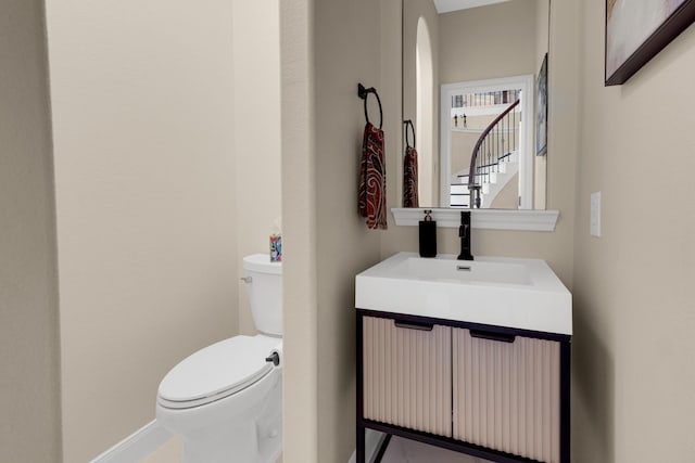 half bathroom with baseboards, vanity, and toilet