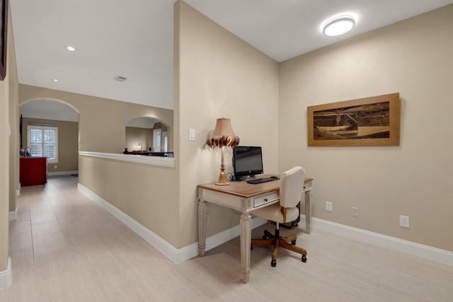 office area with light wood-style floors, baseboards, and arched walkways