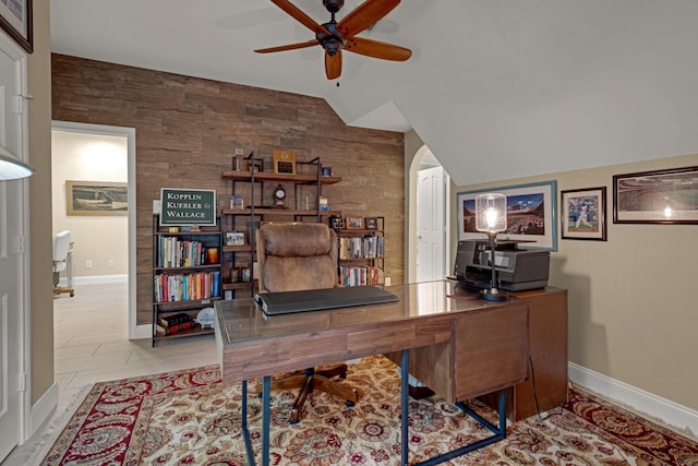 office area featuring arched walkways, an accent wall, a ceiling fan, baseboards, and vaulted ceiling