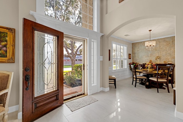 entryway with arched walkways, crown molding, a high ceiling, and an inviting chandelier