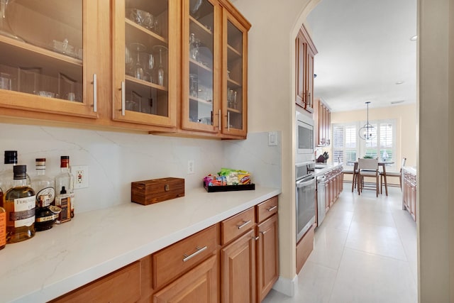 kitchen featuring appliances with stainless steel finishes, pendant lighting, glass insert cabinets, and backsplash