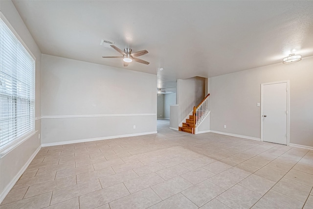 empty room featuring light tile patterned floors, visible vents, baseboards, a ceiling fan, and stairs