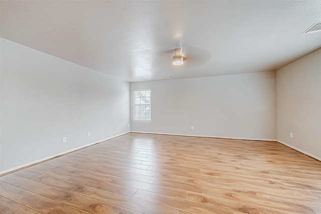 spare room with light wood-type flooring, visible vents, ceiling fan, and baseboards