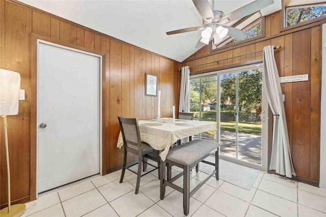 dining space with a ceiling fan, lofted ceiling, wood walls, and light tile patterned floors