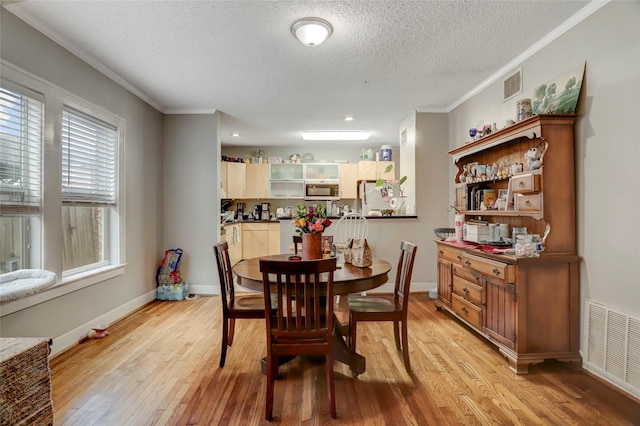 dining room featuring ornamental molding, light wood-style flooring, visible vents, and baseboards