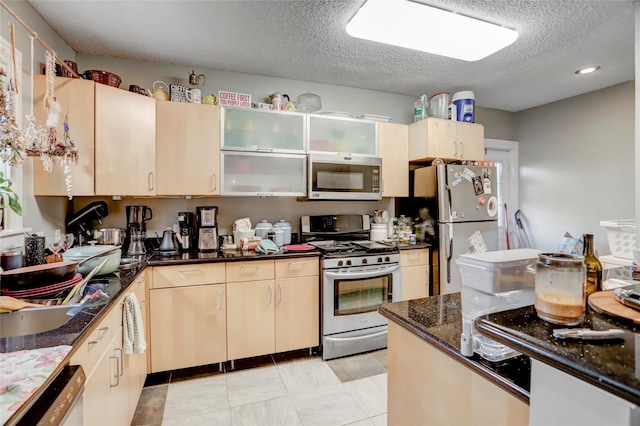 kitchen with appliances with stainless steel finishes, glass insert cabinets, light brown cabinets, a textured ceiling, and dark stone countertops