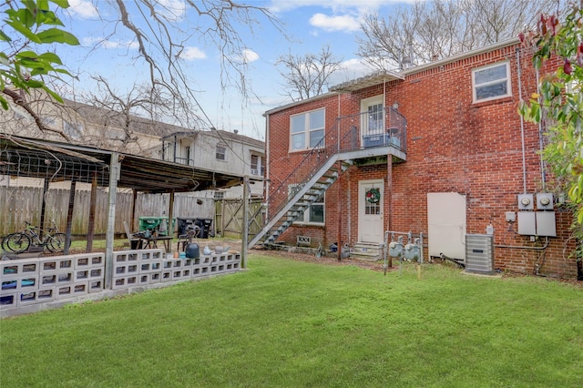 rear view of house with a yard, fence, central AC unit, and brick siding