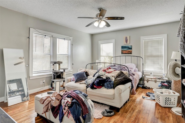 bedroom with light wood-type flooring, ceiling fan, a textured ceiling, and baseboards