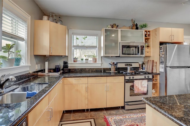 kitchen featuring dark stone countertops, appliances with stainless steel finishes, a sink, and light brown cabinetry