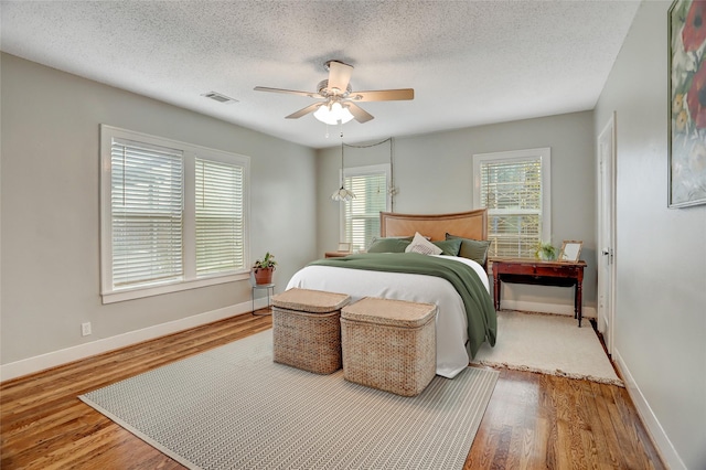 bedroom with a ceiling fan, visible vents, baseboards, and wood finished floors