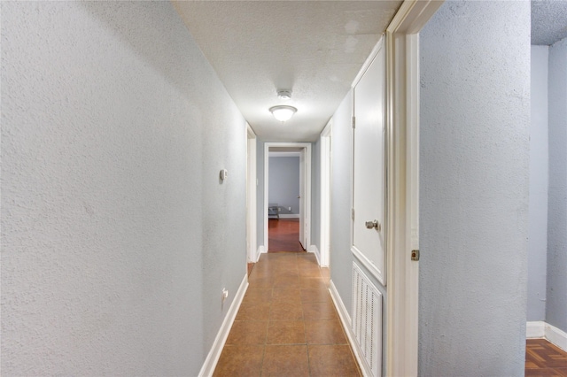 corridor featuring a textured ceiling, a textured wall, visible vents, baseboards, and tile patterned floors