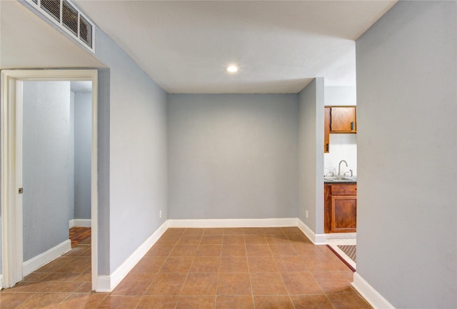 hall with visible vents, a sink, baseboards, and light tile patterned floors