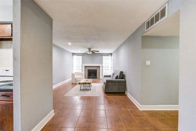 unfurnished living room with visible vents, baseboards, dark tile patterned flooring, a glass covered fireplace, and ceiling fan