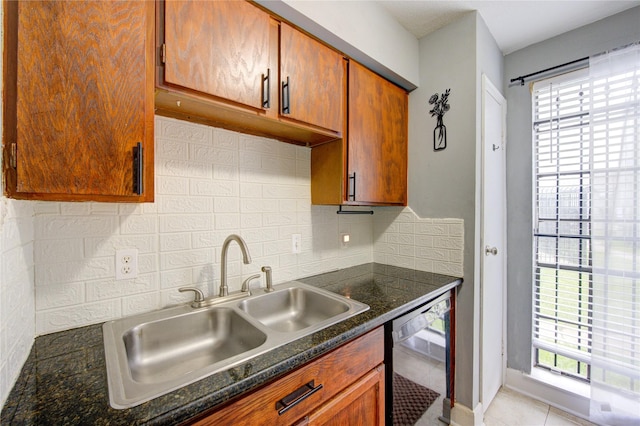 kitchen with dishwasher, dark countertops, backsplash, a sink, and light tile patterned flooring