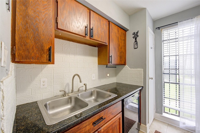 kitchen featuring light tile patterned floors, a sink, black dishwasher, backsplash, and dark countertops