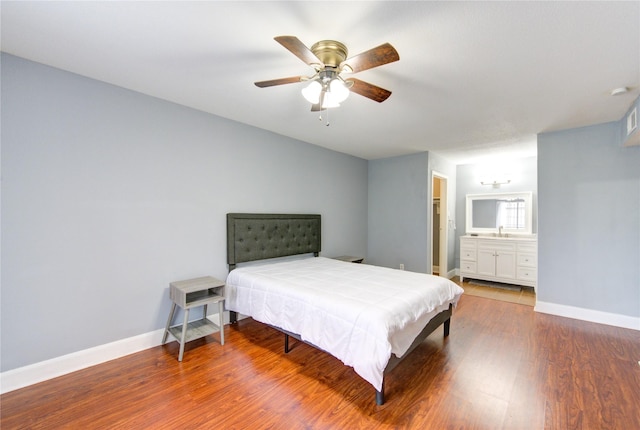 bedroom featuring ceiling fan, connected bathroom, a sink, wood finished floors, and baseboards