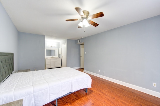 bedroom featuring baseboards, ceiling fan, wood finished floors, ensuite bathroom, and a sink