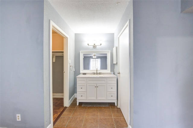 bathroom with baseboards, tile patterned flooring, a spacious closet, a textured ceiling, and vanity