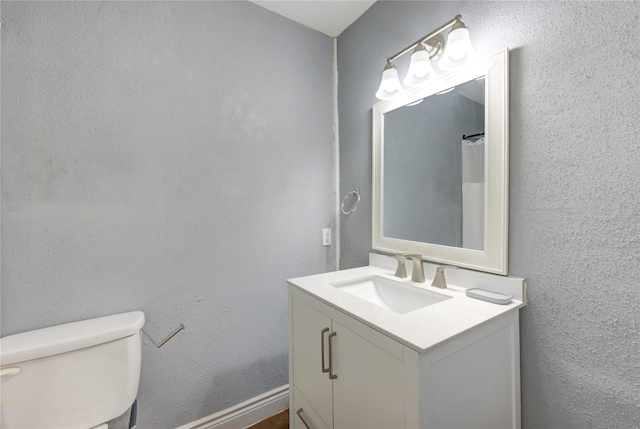 bathroom with a textured wall, vanity, and toilet