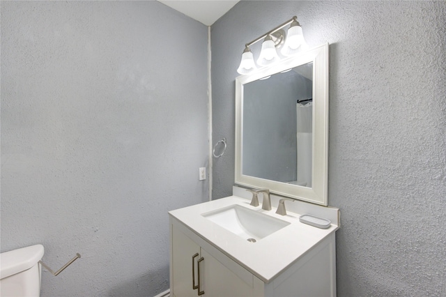 full bath with toilet, a textured wall, and vanity