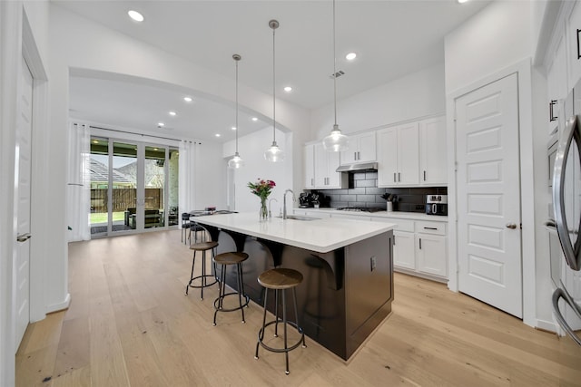 kitchen featuring gas stovetop, light wood-style flooring, backsplash, a sink, and under cabinet range hood