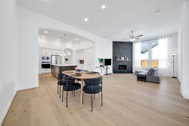 dining area with arched walkways, a fireplace, recessed lighting, light wood-style flooring, and ceiling fan