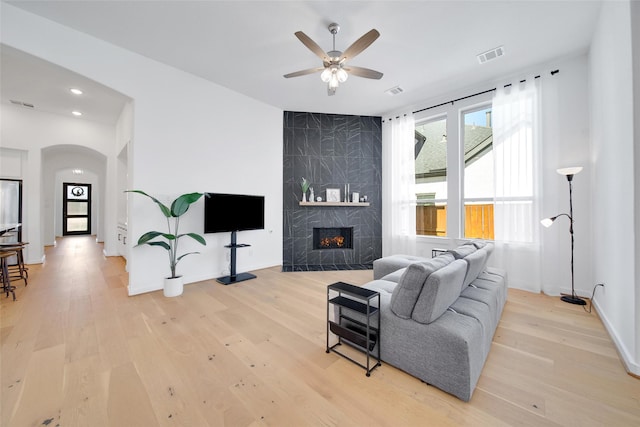 living area with light wood-style flooring, a premium fireplace, visible vents, and arched walkways