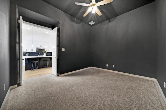 spare room featuring a ceiling fan, light carpet, and baseboards